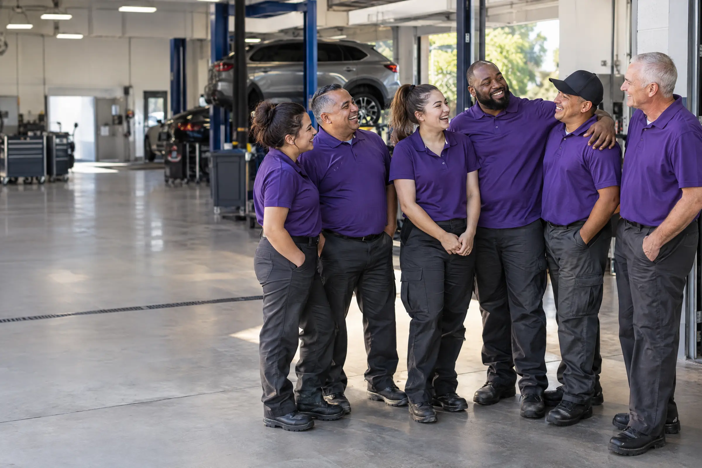 A team of associates and technicians in purple polos laugh together in the doorway of a service bay