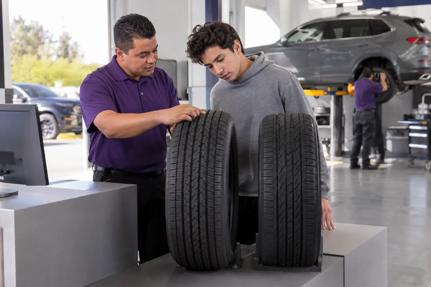 A store associate helps a young customer compare two tires at the counter