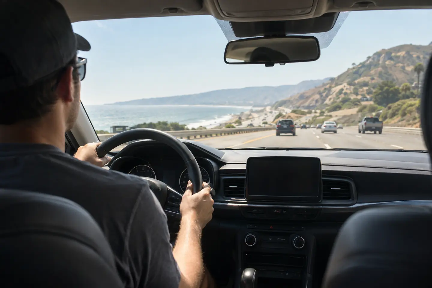 A driver’s hands on the steering wheel on a straight coastal highway