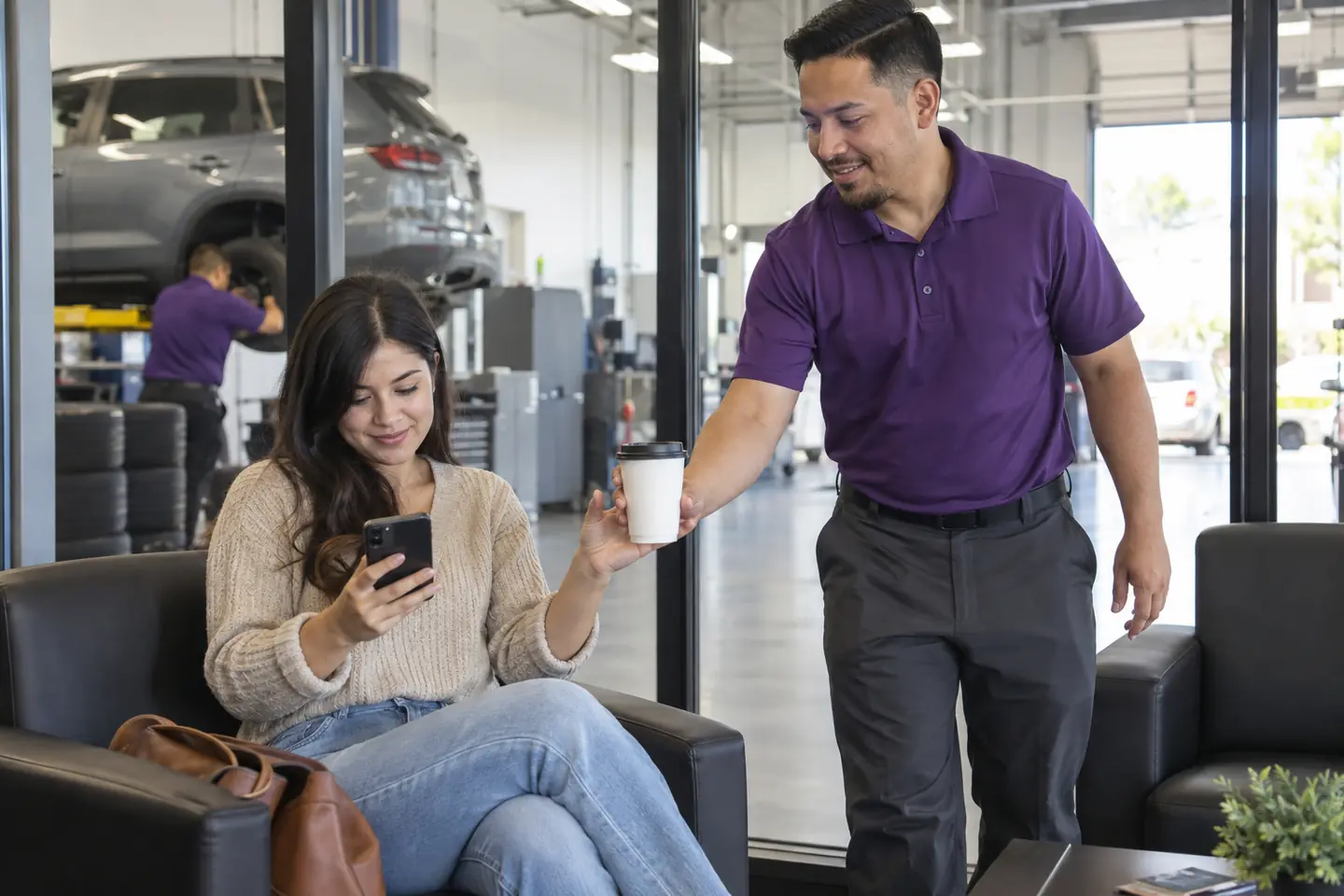 A customer compares tire prices on her phone in the waiting area as an associate brings her a coffee