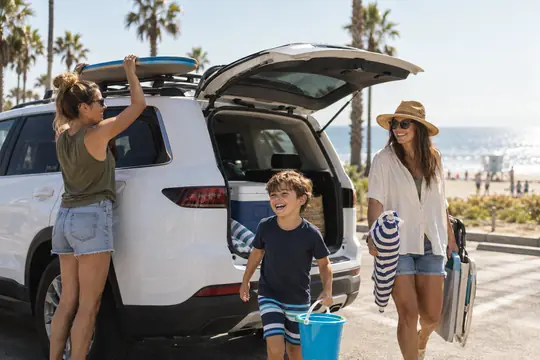 Two moms and their son unloading beach gear from their SUV by the ocean
