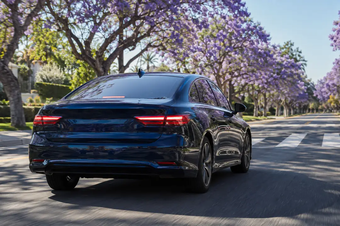 A sedan slowing to a stop on a street lined with jacaranda trees