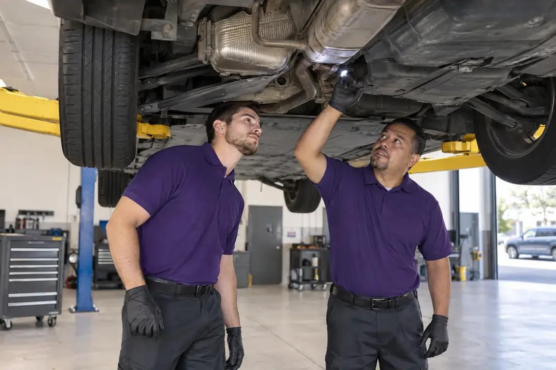 Two technicians inspecting the underside of a minivan