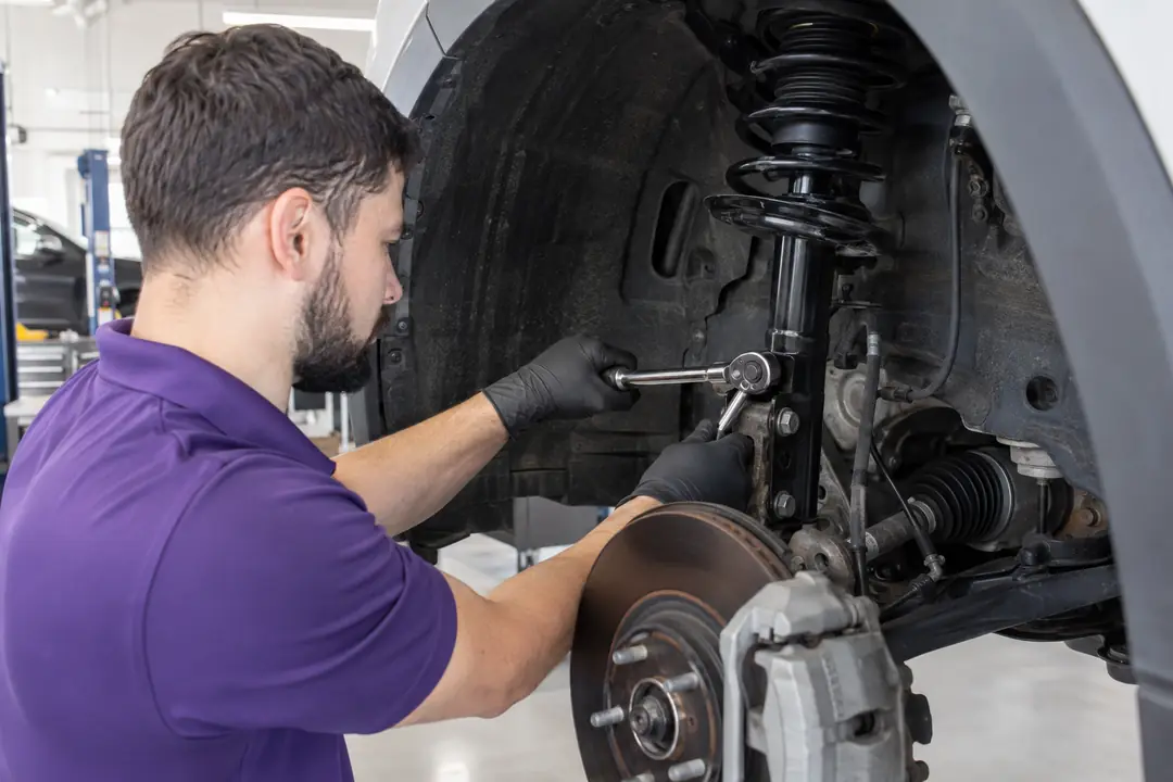 Gloved hands tightening the bolts of a new strut to the steering knuckle