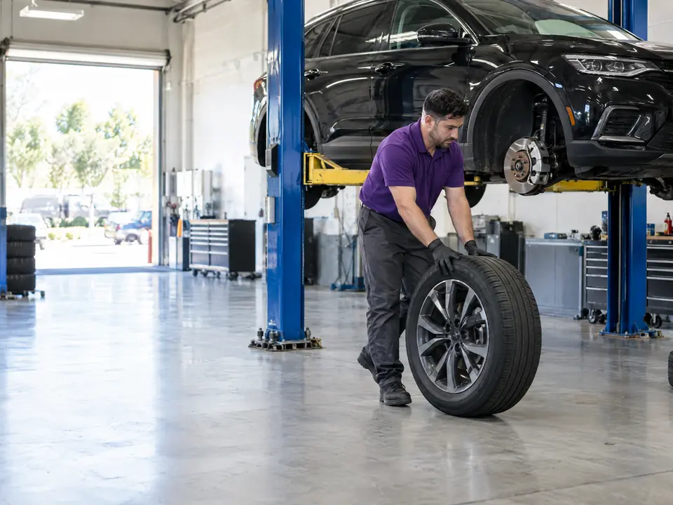 A technician rolling a wheel beside a crossover raised on a lift