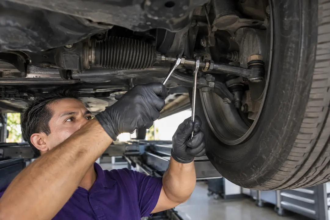 Gloved hands adjusting a tie rod with two wrenches